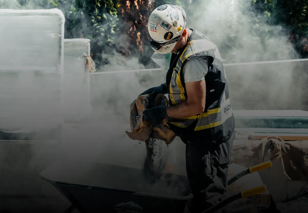 A crew member pouring a bag of concrete mix into a wheelbarrow on a job site